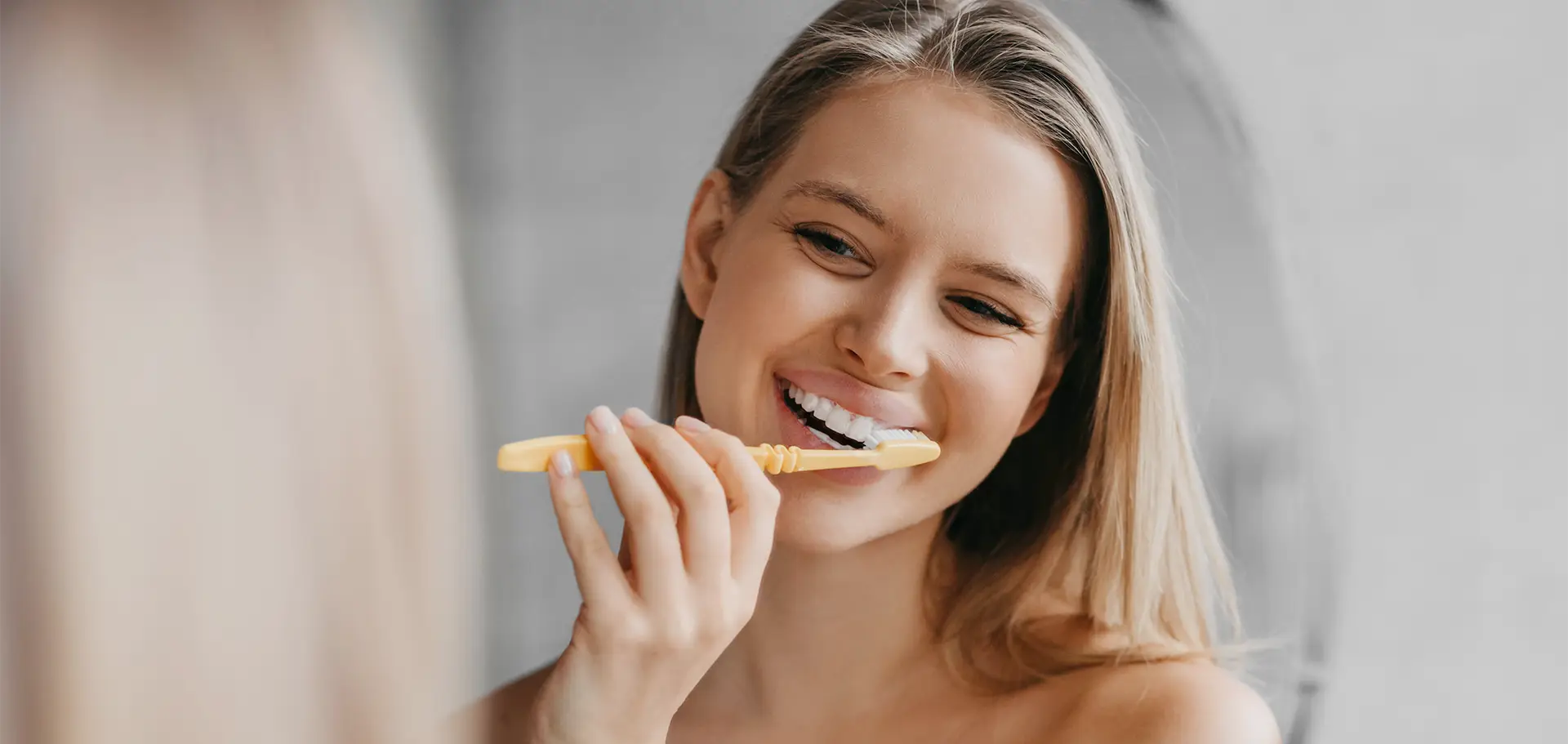 uśmiechnięta kobieta myjąca zęby przed lustrem